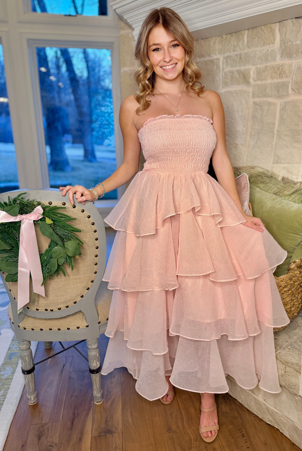 Woman in a pink strapless dress standing in a room with a decorative chair and wreath.
