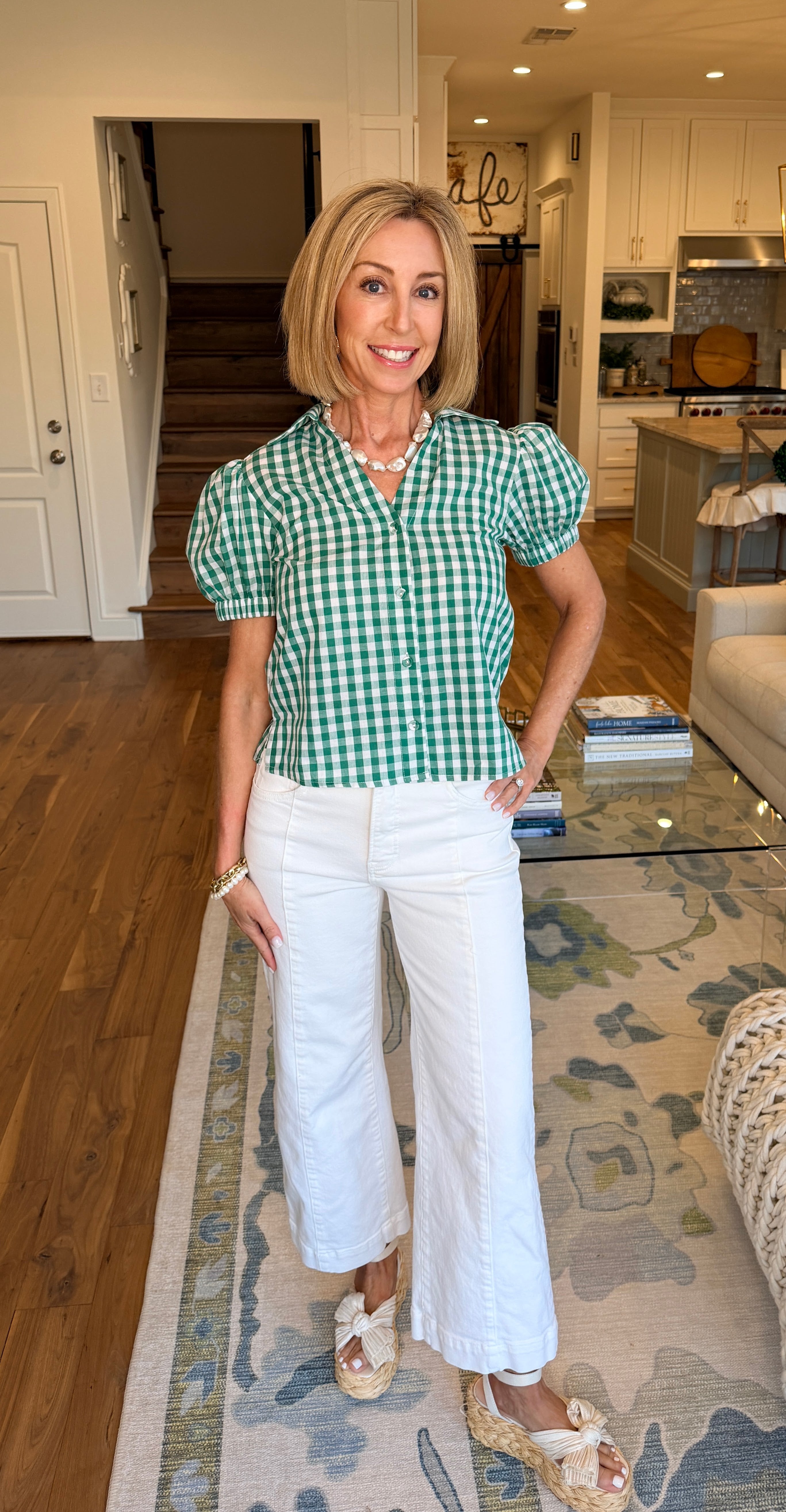 Woman in a green checkered shirt and white pants standing in a home interior.